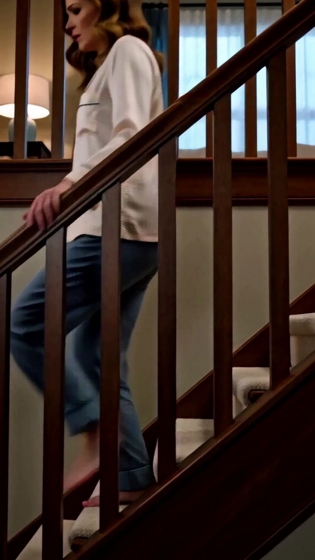 A woman in pajamas hurries barefoot down a wooden staircase.